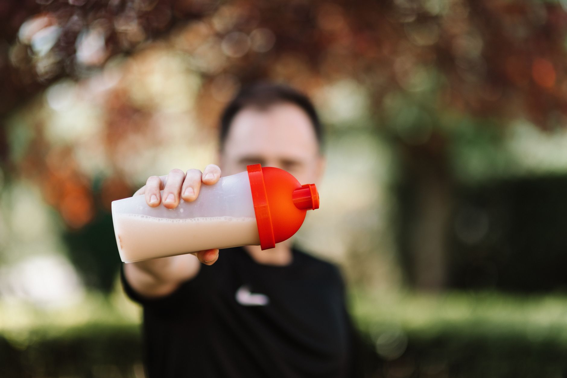 A person pouring whey protein powder into a shaker bottle.